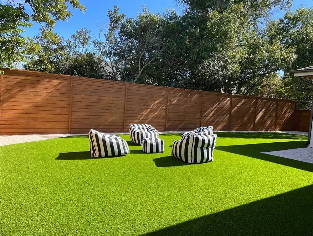 Bright artificial turf backyard with lounge chairs and a cedar fence, installed by hello TURF in Austin